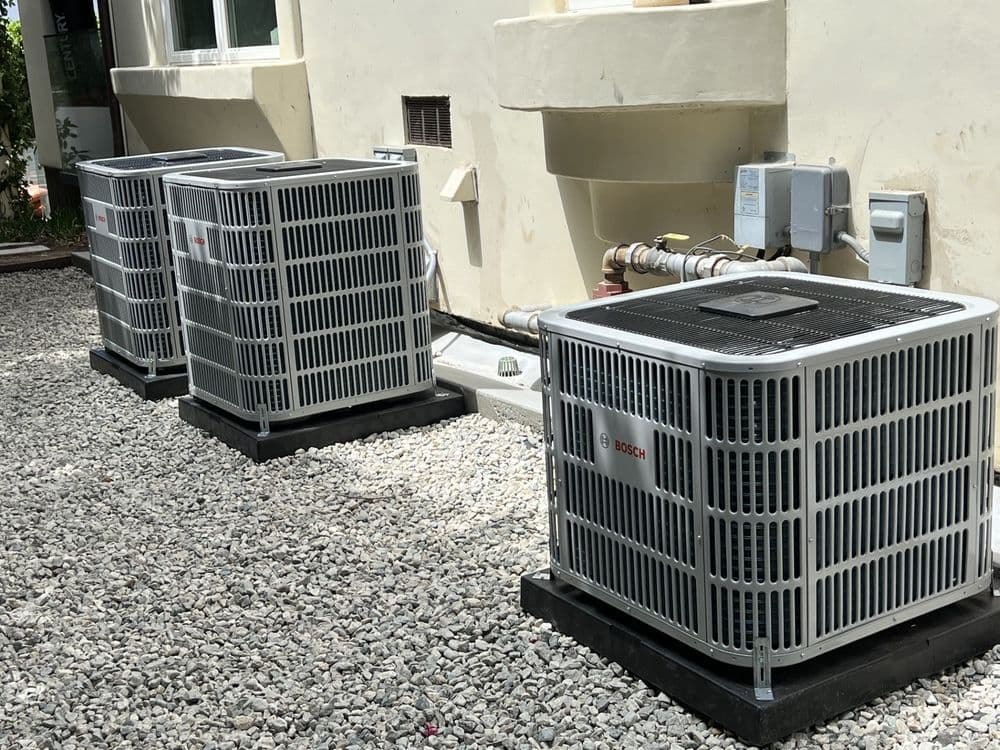 Three Bosch air conditioning units installed on a gravel surface near a building.