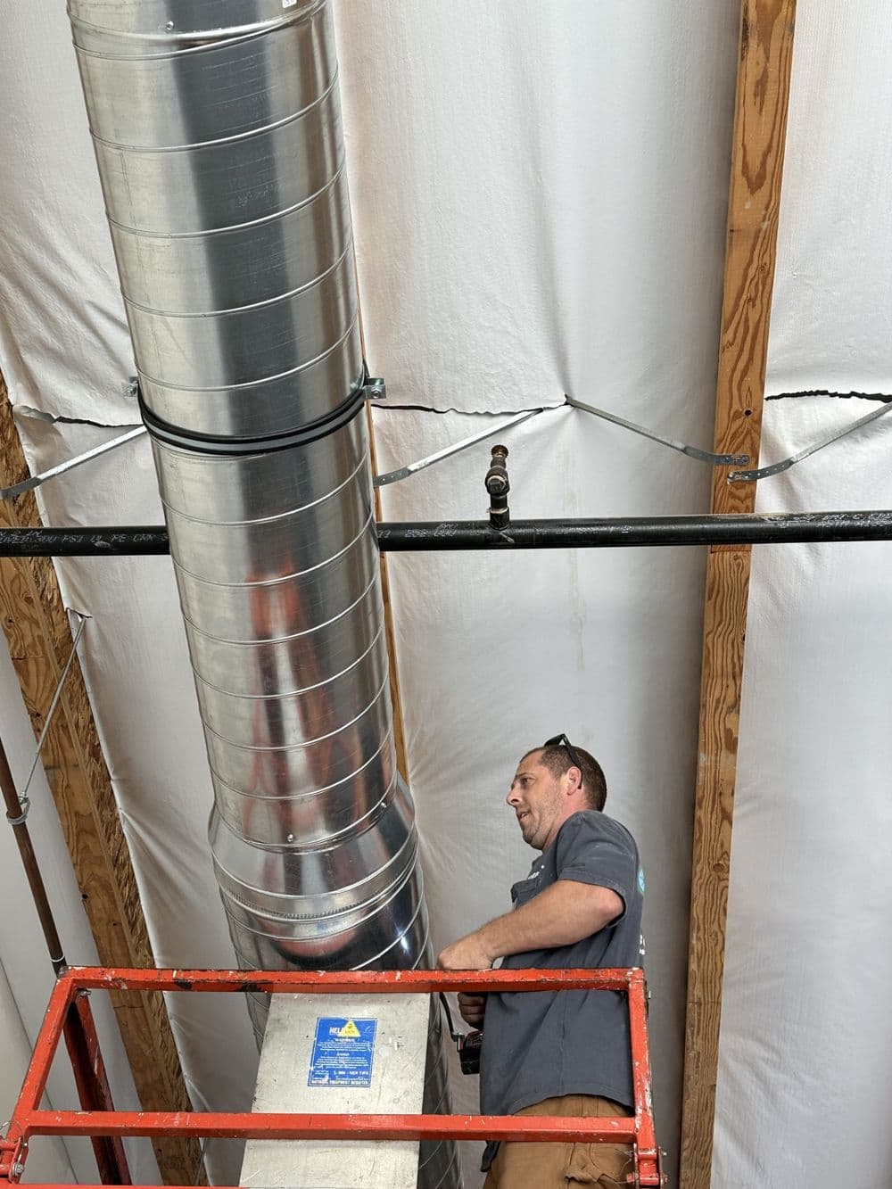 Technician installing ductwork on scaffolding in a commercial building ceiling.