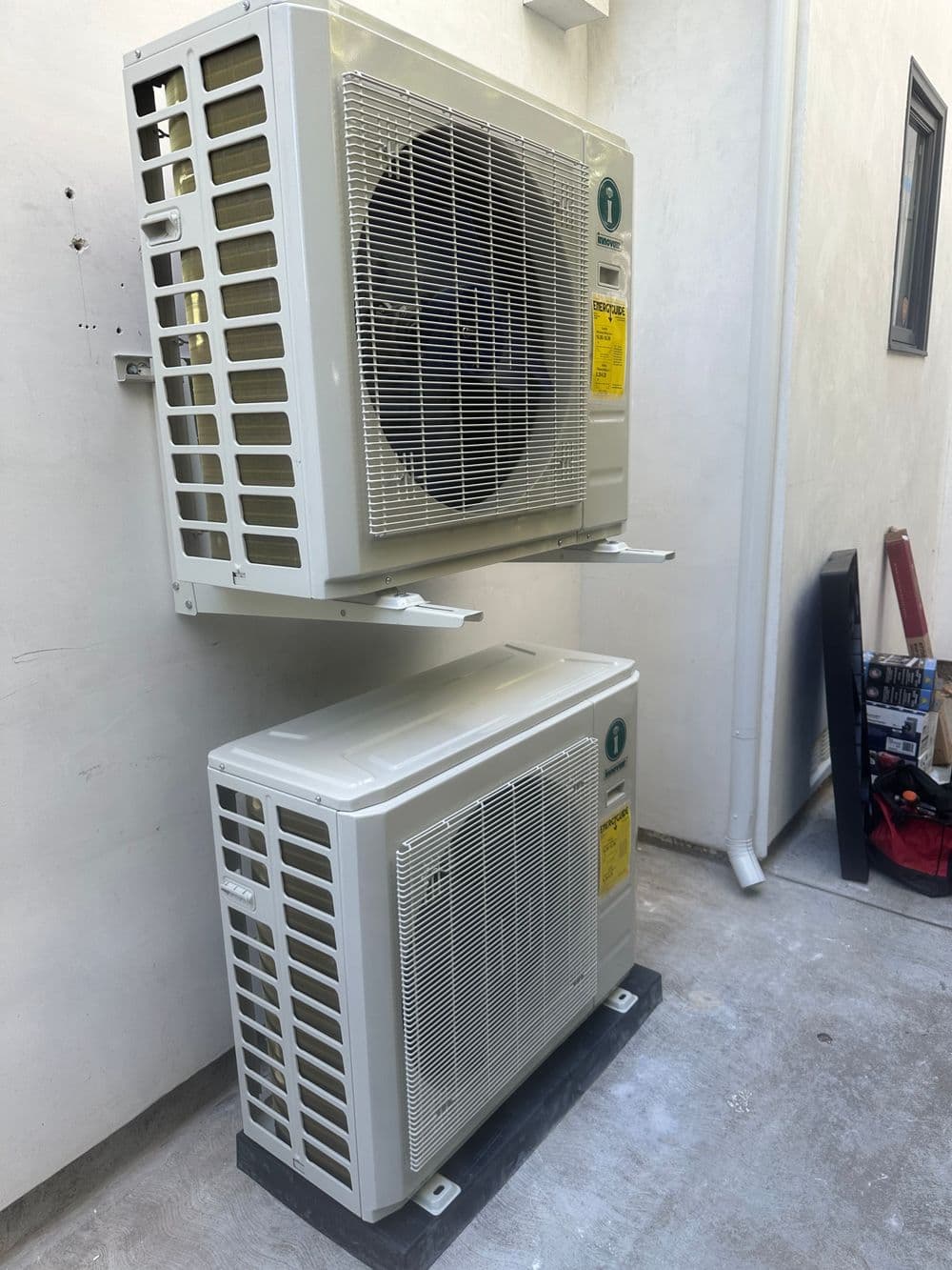 Two outdoor air conditioning units mounted on a wall with visible electrical labels and plumbing.