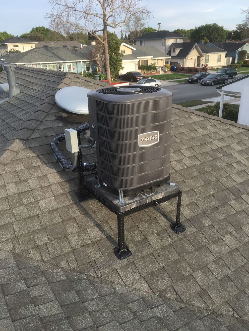Maytag HVAC unit installed on a residential roof with shingles and surrounding houses.