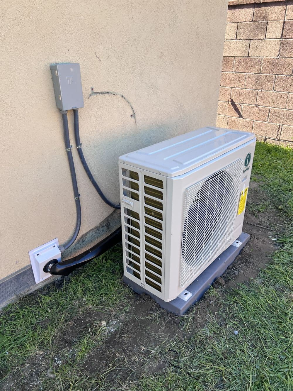 Air conditioning unit installed on exterior wall with connecting pipes and electrical panel.