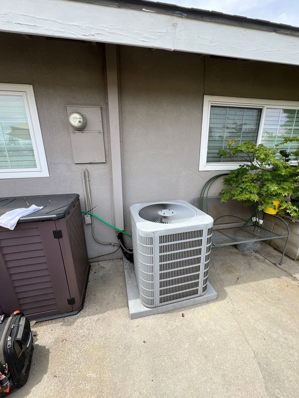 Air conditioning unit installed beside a house, with utility meter and garden feature visible.