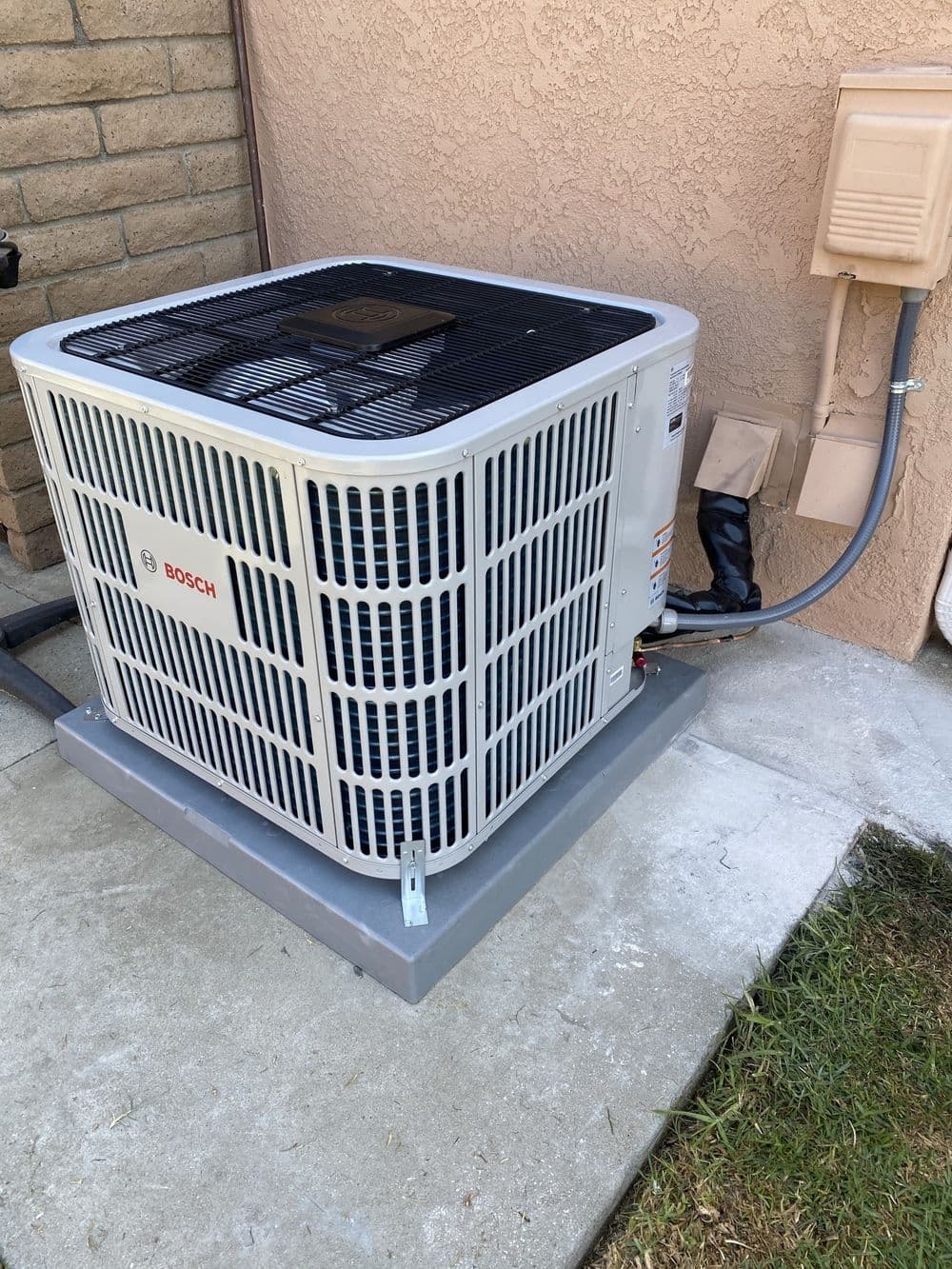 Bosch air conditioning unit installed outside a building on a concrete pad.