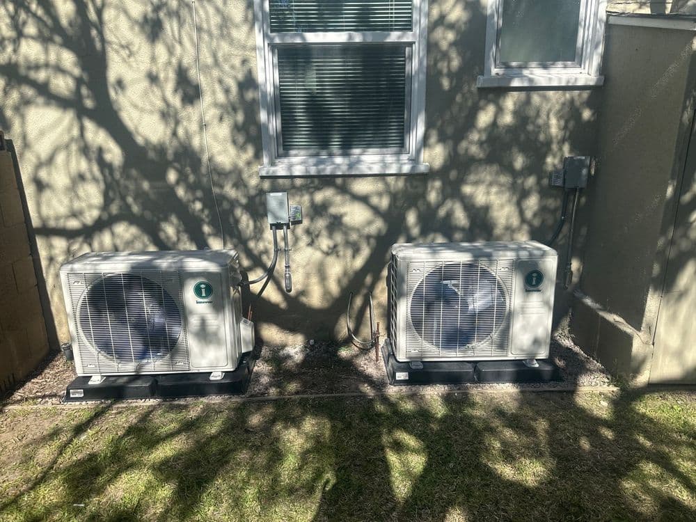 Air conditioning units installed beside a house, casting shadows on the wall.