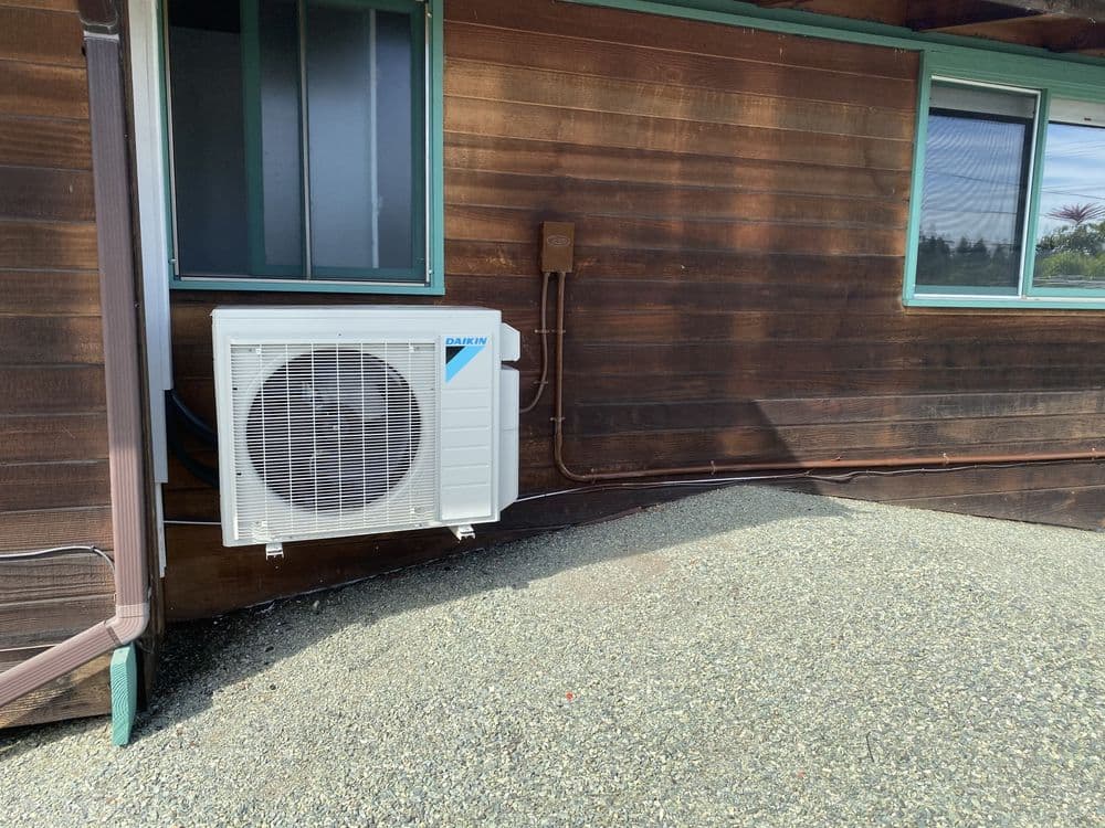 Ductless air conditioning unit installed on a wooden exterior wall with gravel surface.