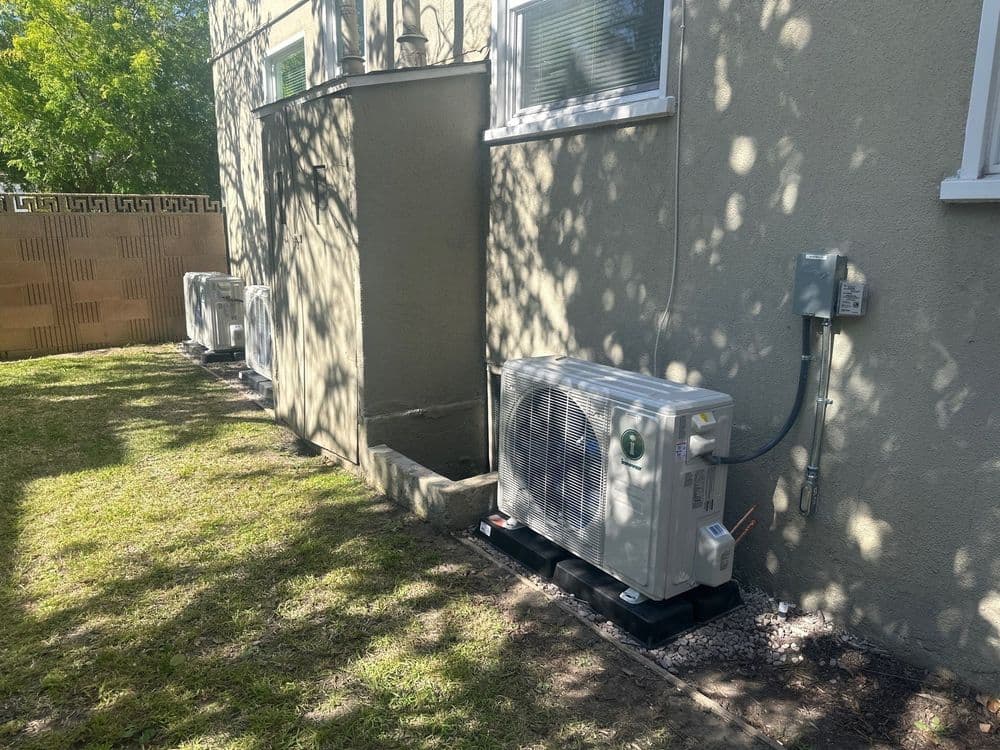 Multiple outdoor air conditioning units installed beside a home's exterior wall in a landscaped area.
